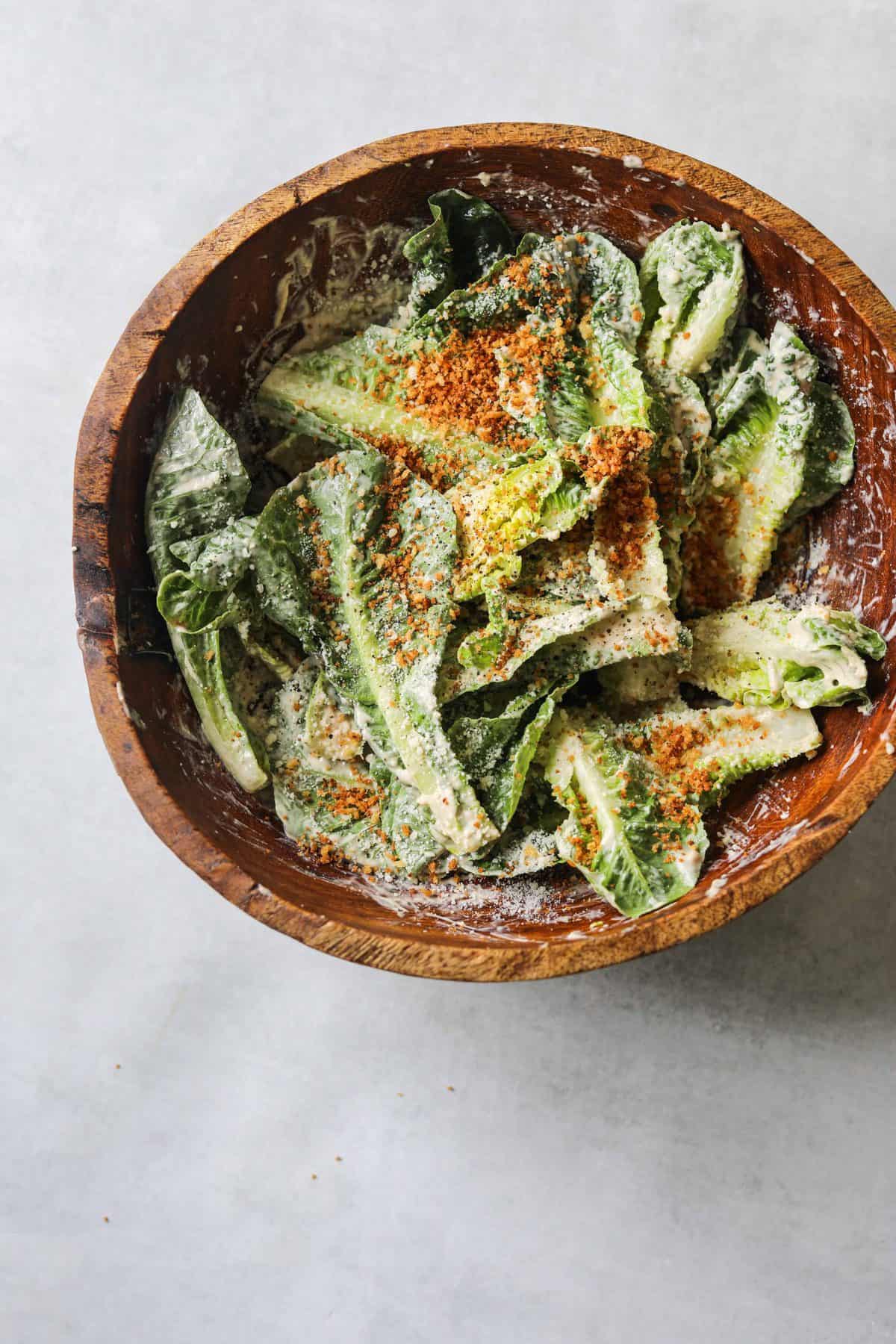 a wooden salad bowl filled with romaine lettuce tossed with Creamy Tahini Caesar Dressing