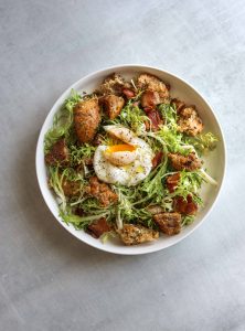 a white bowl filled with Frisée Salad with Bacon, Croutons, and Poached Egg