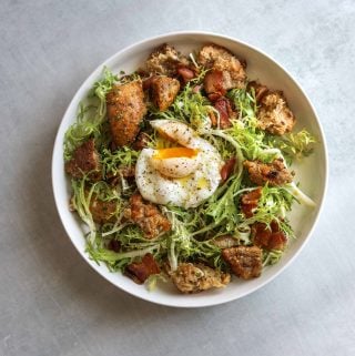 a white bowl filled with Frisée Salad with Bacon, Croutons, and Poached Egg