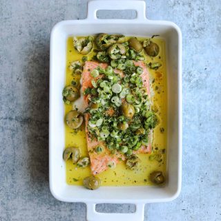 Slow Roasted Salmon in a baking dish with topped with green olive salsa verde