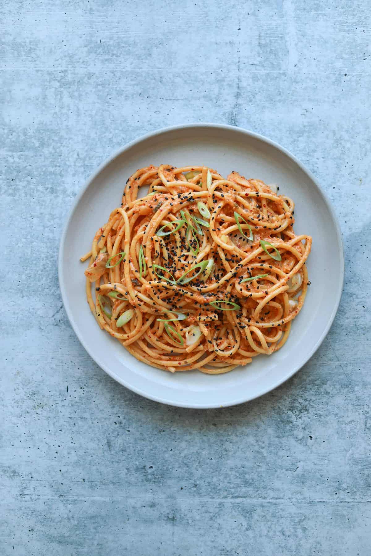 Kimchi Carbonara on a white plate with sesame seeds and scallions