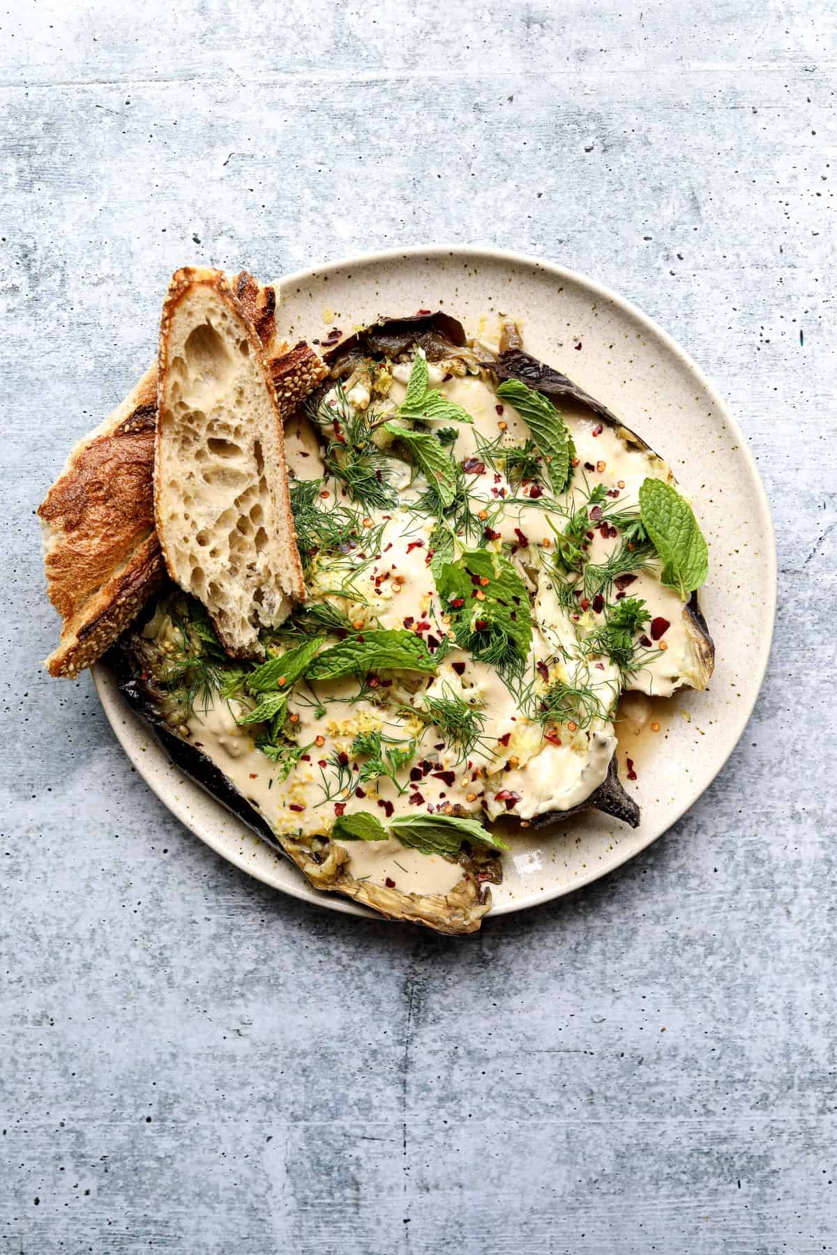 Whole Roasted Eggplant with Garlic Tahini on a plate with toasted bread