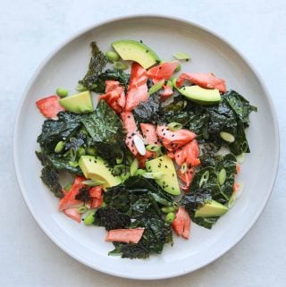 kale salad on a plate with salmon, avocado and sesame seeds