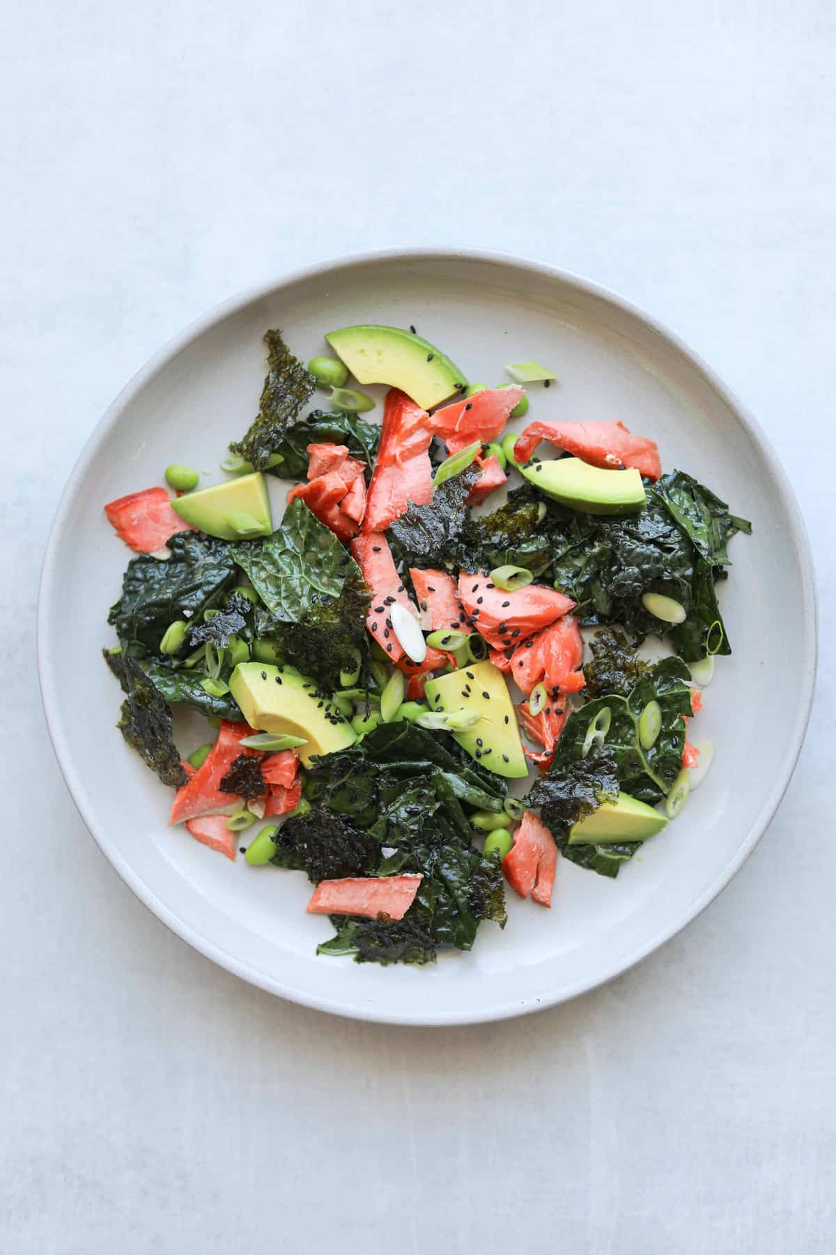 kale salad on a plate with salmon, avocado and sesame seeds