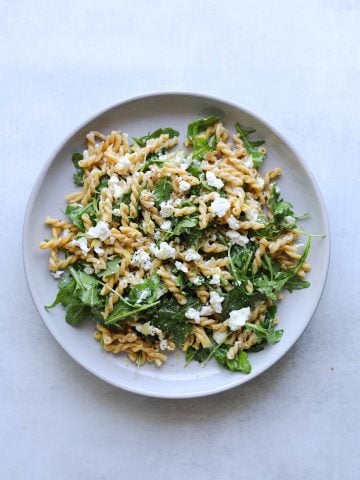 chickepea pasta with arugula and feta on a white plate