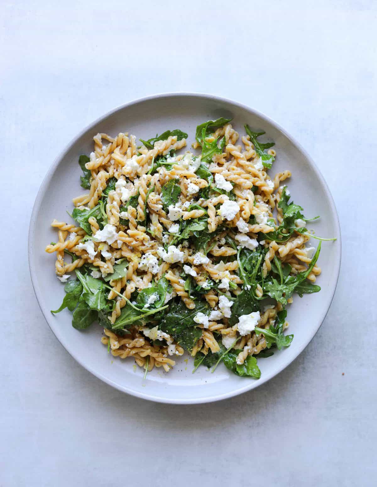 chickepea pasta with arugula and feta on a white plate