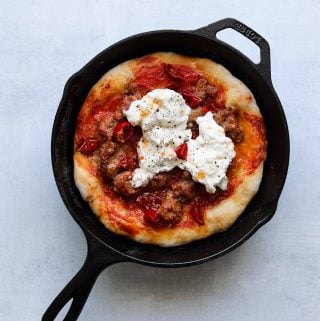 pizza in a cast iron pan topped with sausage, chilis and burrata
