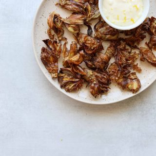 fried artichokes on a plate with aioli on a blue background