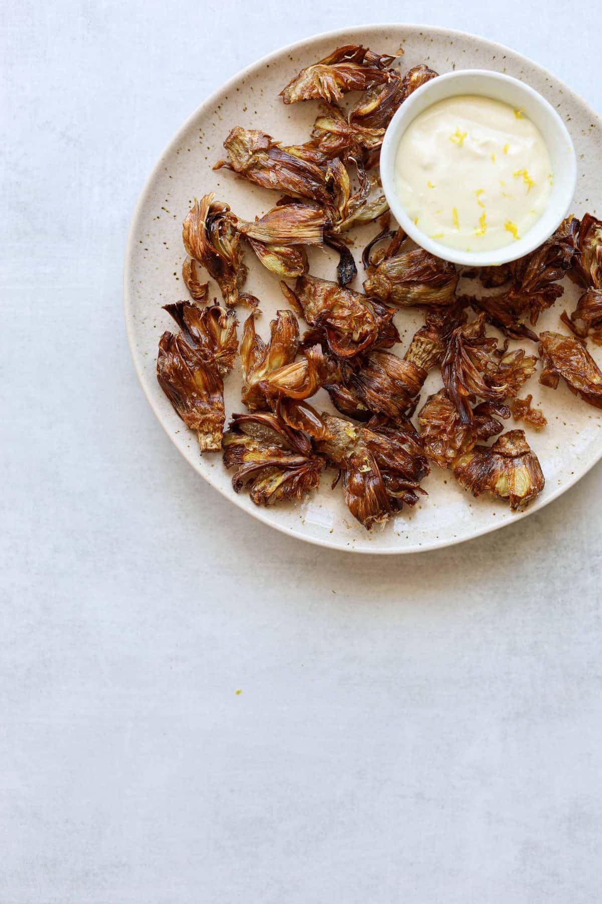 fried artichokes on a plate with aioli on a blue background