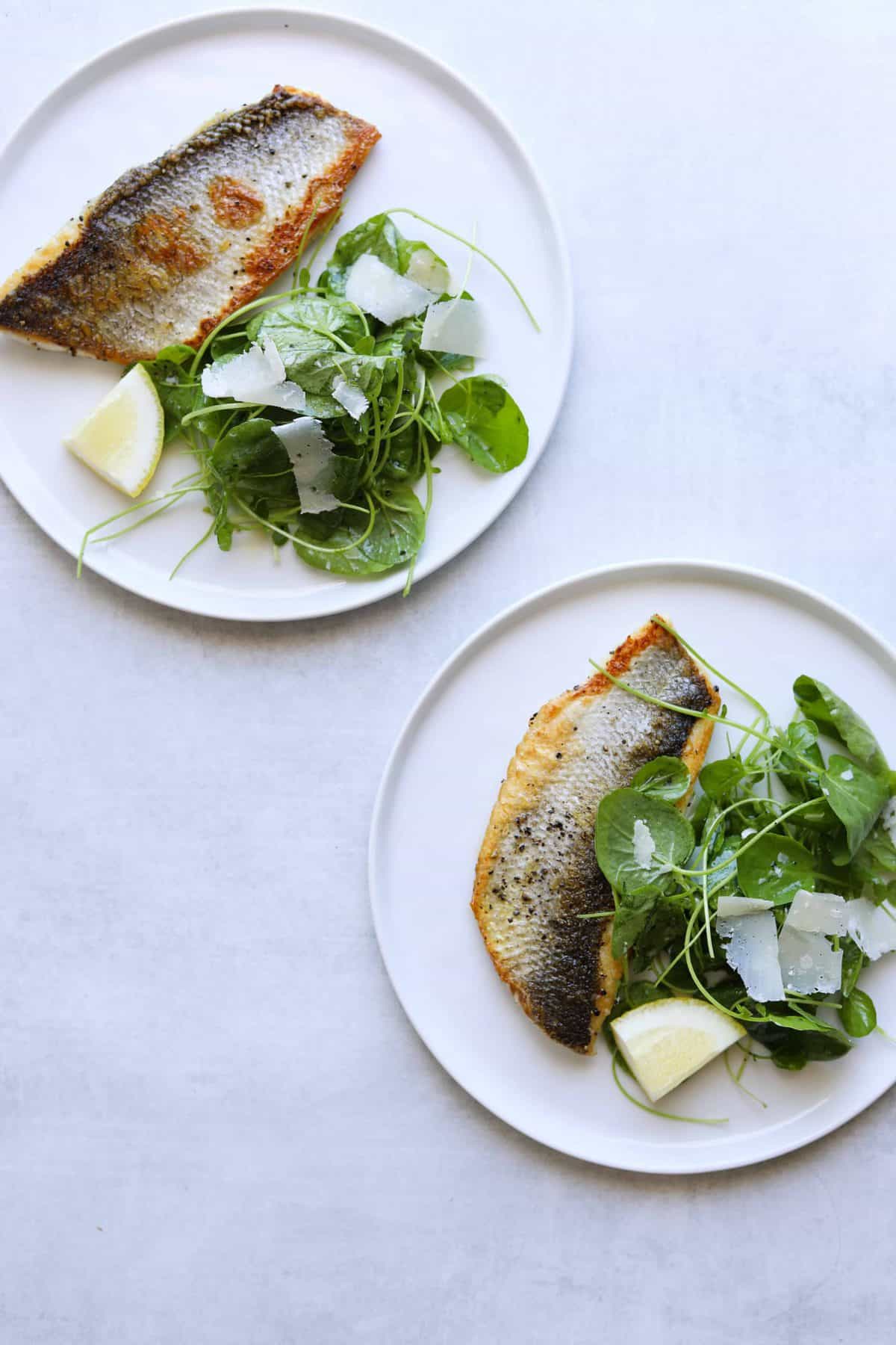 two plates with a filet of crispy skin branzino and watercress salad