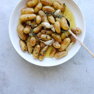 Roasted Fingerling Potatoes with Garlic and Rosemary in a white bowl with a gold spoon