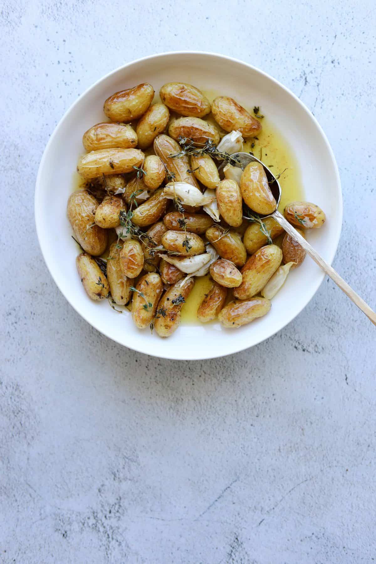 Roasted Fingerling Potatoes with Garlic and Rosemary in a white bowl with a gold spoon