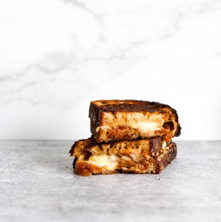 A stack of two pieces of melty grilled cheese with caramelized onions on a grey background.