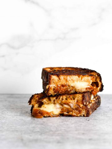 A stack of two pieces of melty grilled cheese with caramelized onions on a grey background.