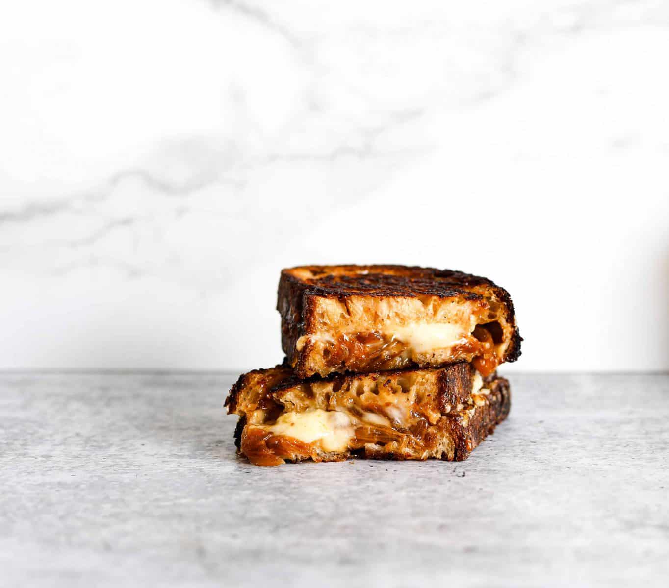 A stack of two pieces of melty grilled cheese with caramelized onions on a grey background.