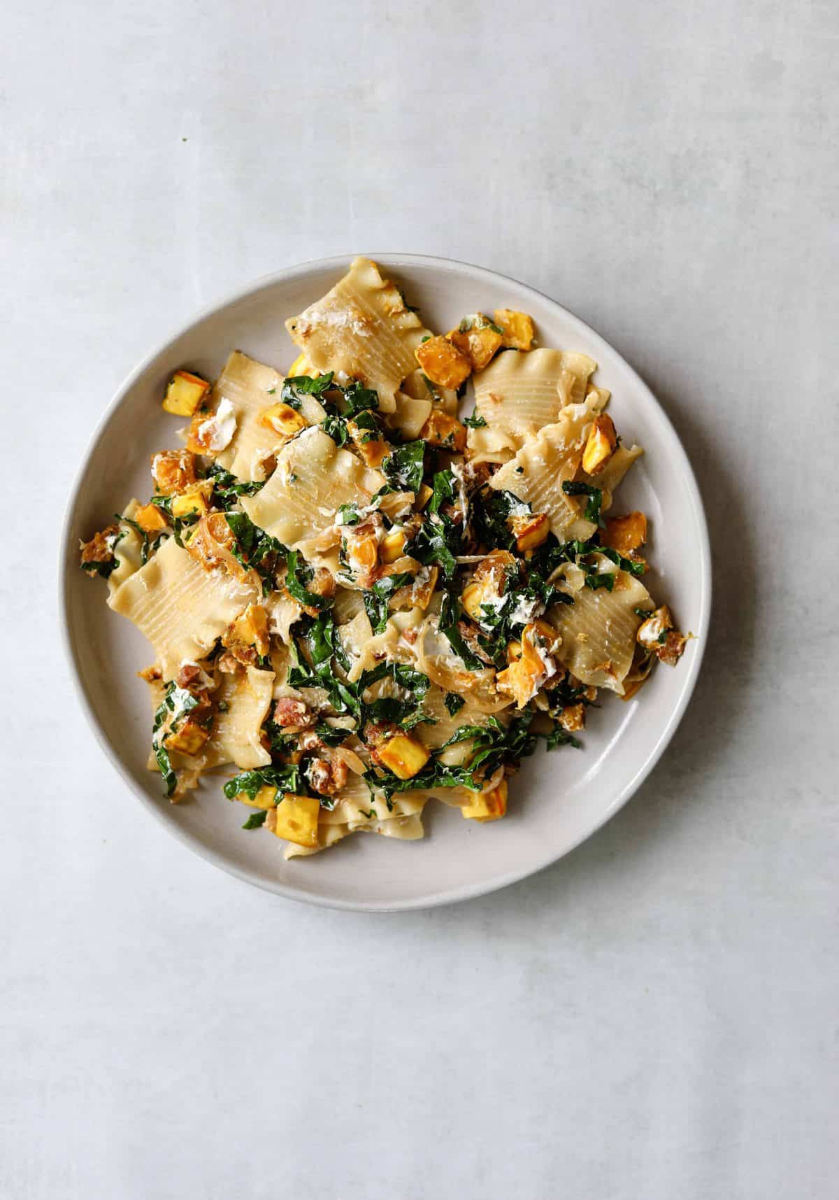 The Perfect Fall Pasta with Pancetta, Squash, Goat Cheese + Kale on a white plate