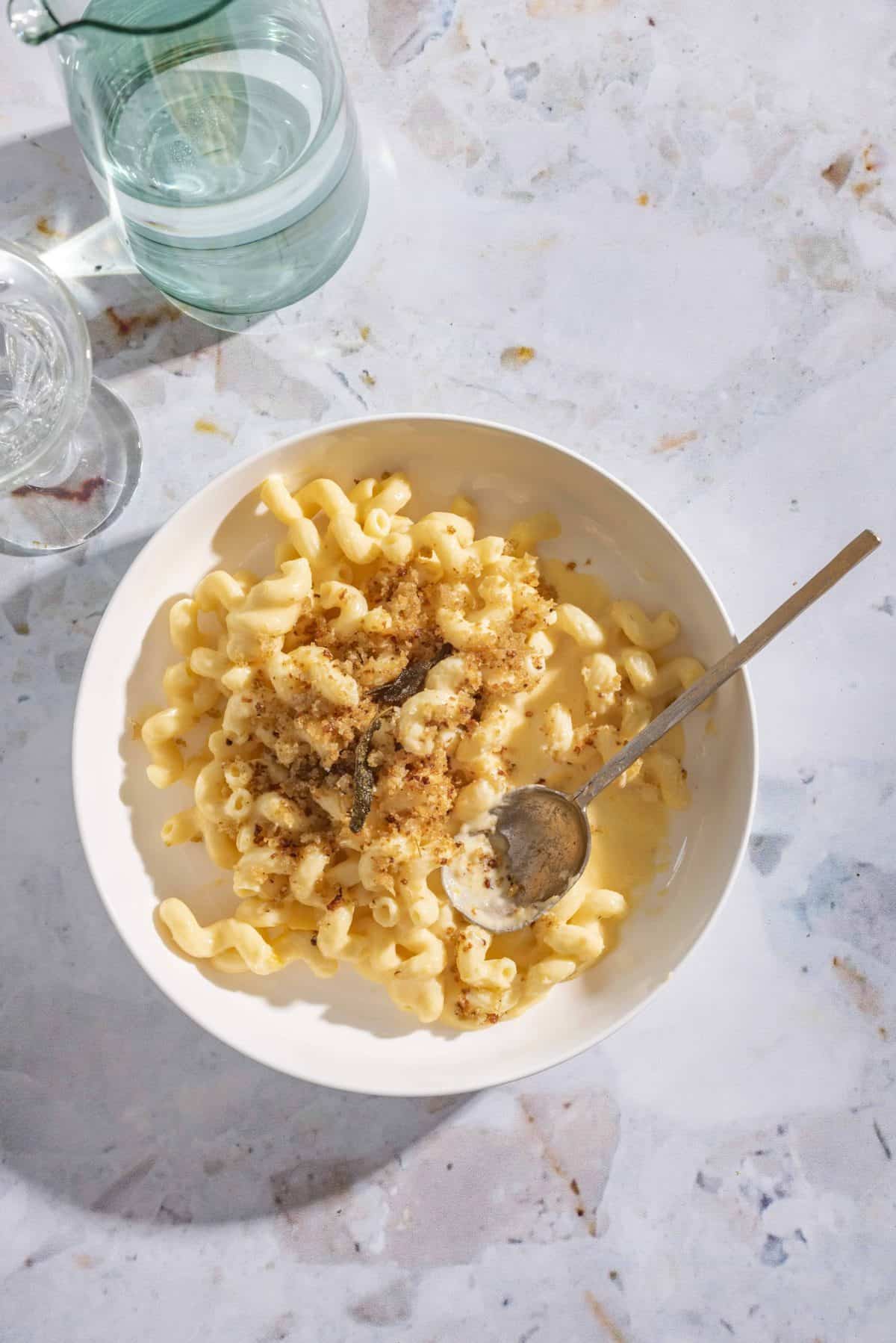 butternut squash mac and cheese topped with crispy sage breadcrumbs in a bowl with a gold spoon