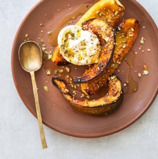 Honey Roasted Squash with Burrata and Pumpkin Seed Dukkah on a brown plate with a gold spoon