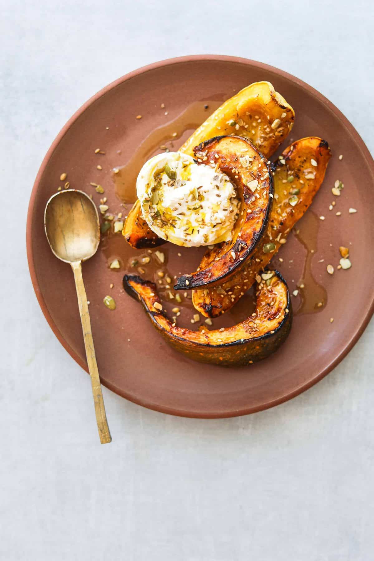 Honey Roasted Squash with Burrata and Pumpkin Seed Dukkah on a brown plate with a gold spoon