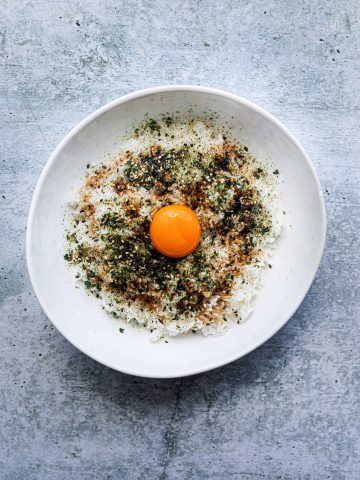 a white bowl with rice, furikake seasoning and an egg yolk