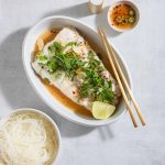 Steamed Halibu in a white serving dish with garlic-lime sauce and rice noodles