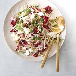 Farro salad on a white plate with gold serving utensils