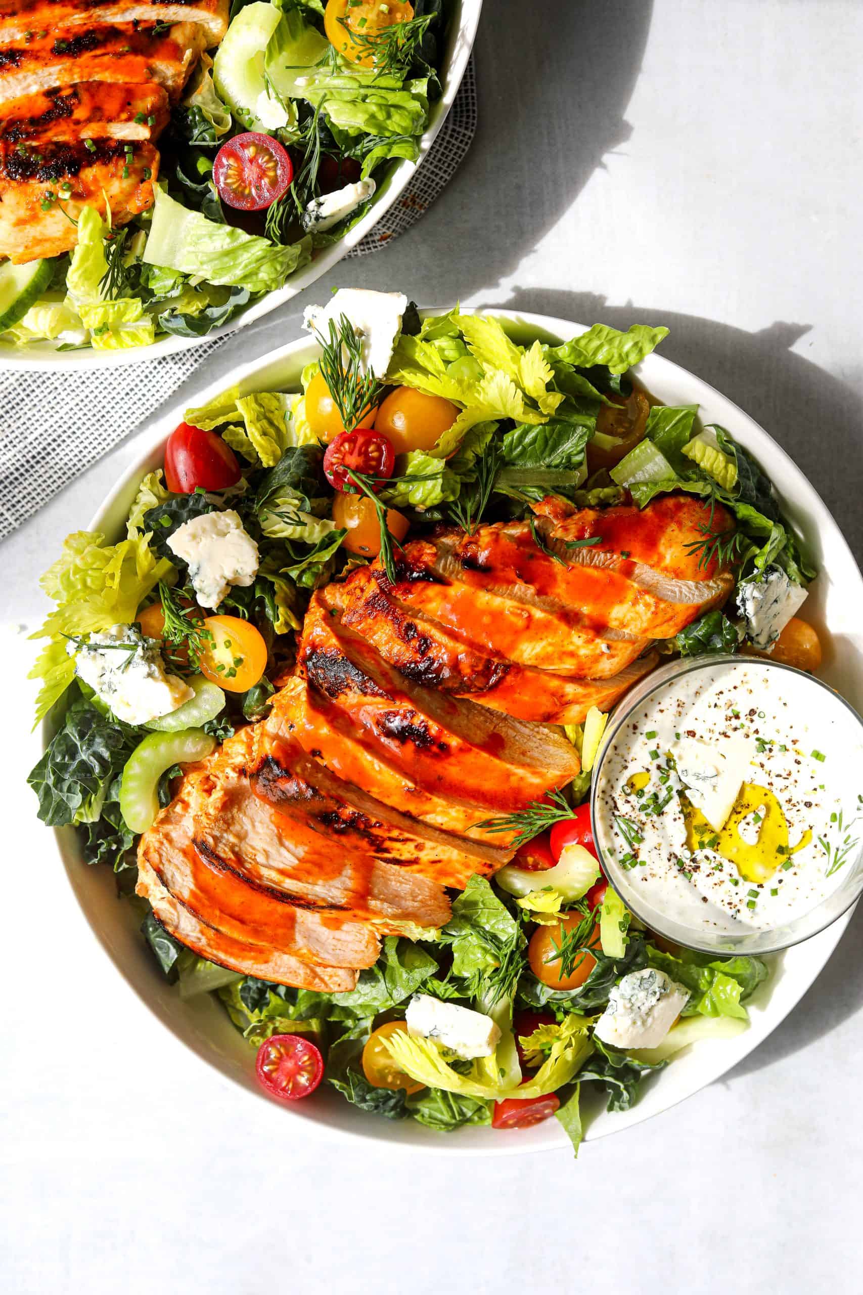 two bowls of salad filled with chopped romaine lettuce, grilled buffalo chicken and crumbled blue cheese