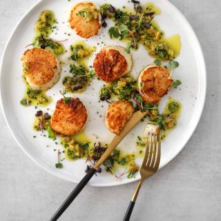 six seared scallops on a plate drizzled with preserved lemon and herb dressing
