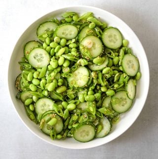 Edamame salad in a white bowl on a blue background.