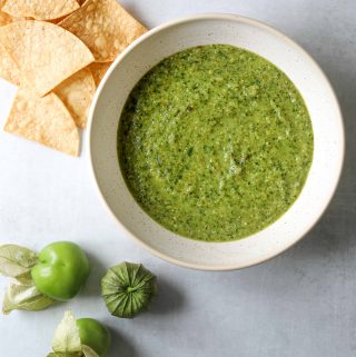 Tomatillo Salsa in a white bowl with tortilla chips and tomatillos