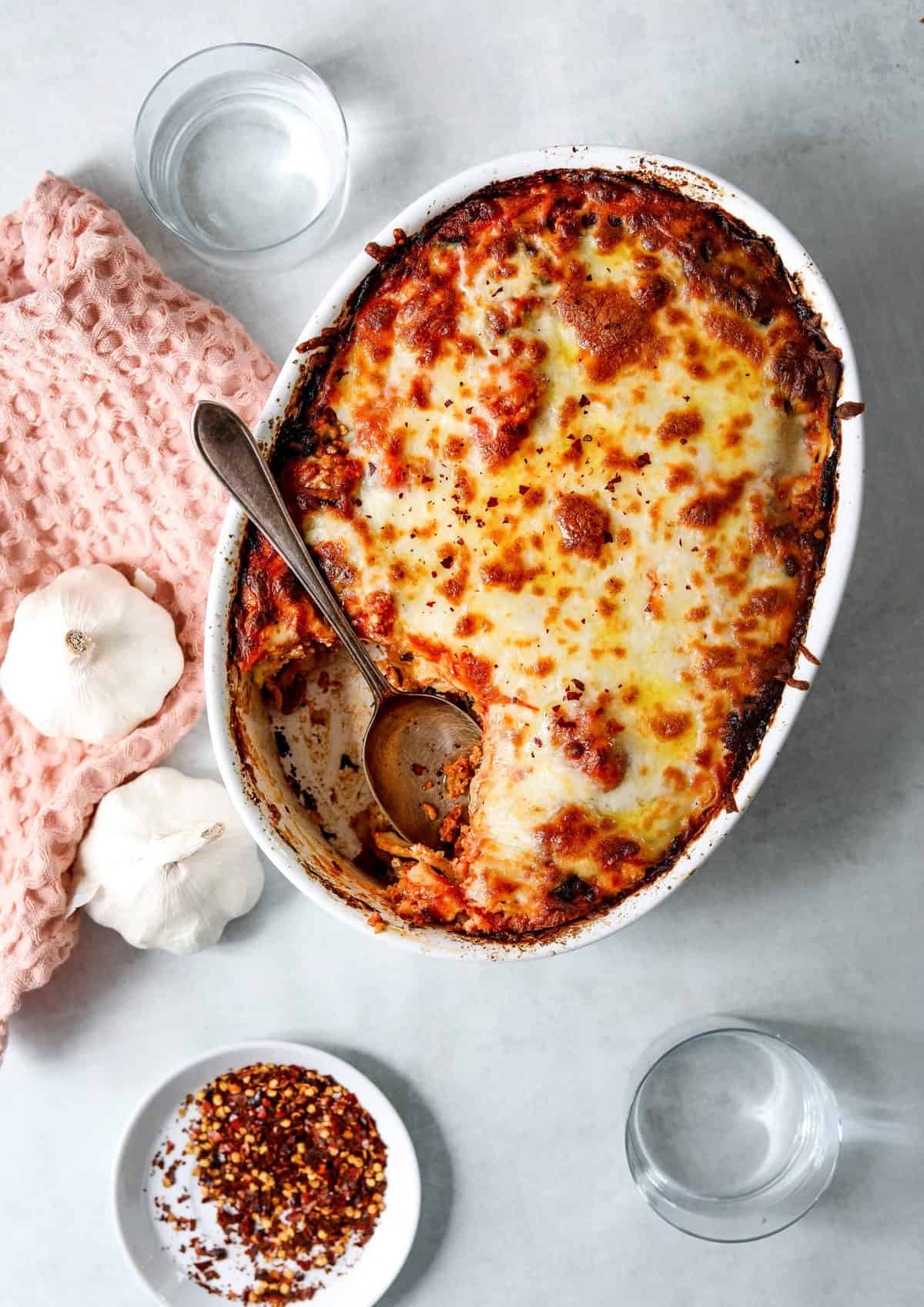 Easy Sausage + Spinach Lasagna with a silver spoon, two bulbs of garlic and a pink kitchen towel