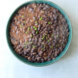 a teal bowl with black beans topped with diced jalapeño