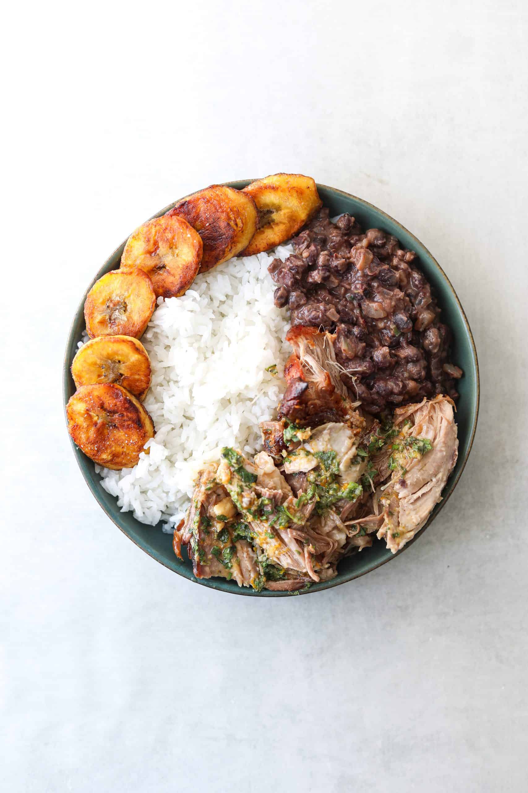 A bowl of mojo pork, white rice, black beans and fried plantains