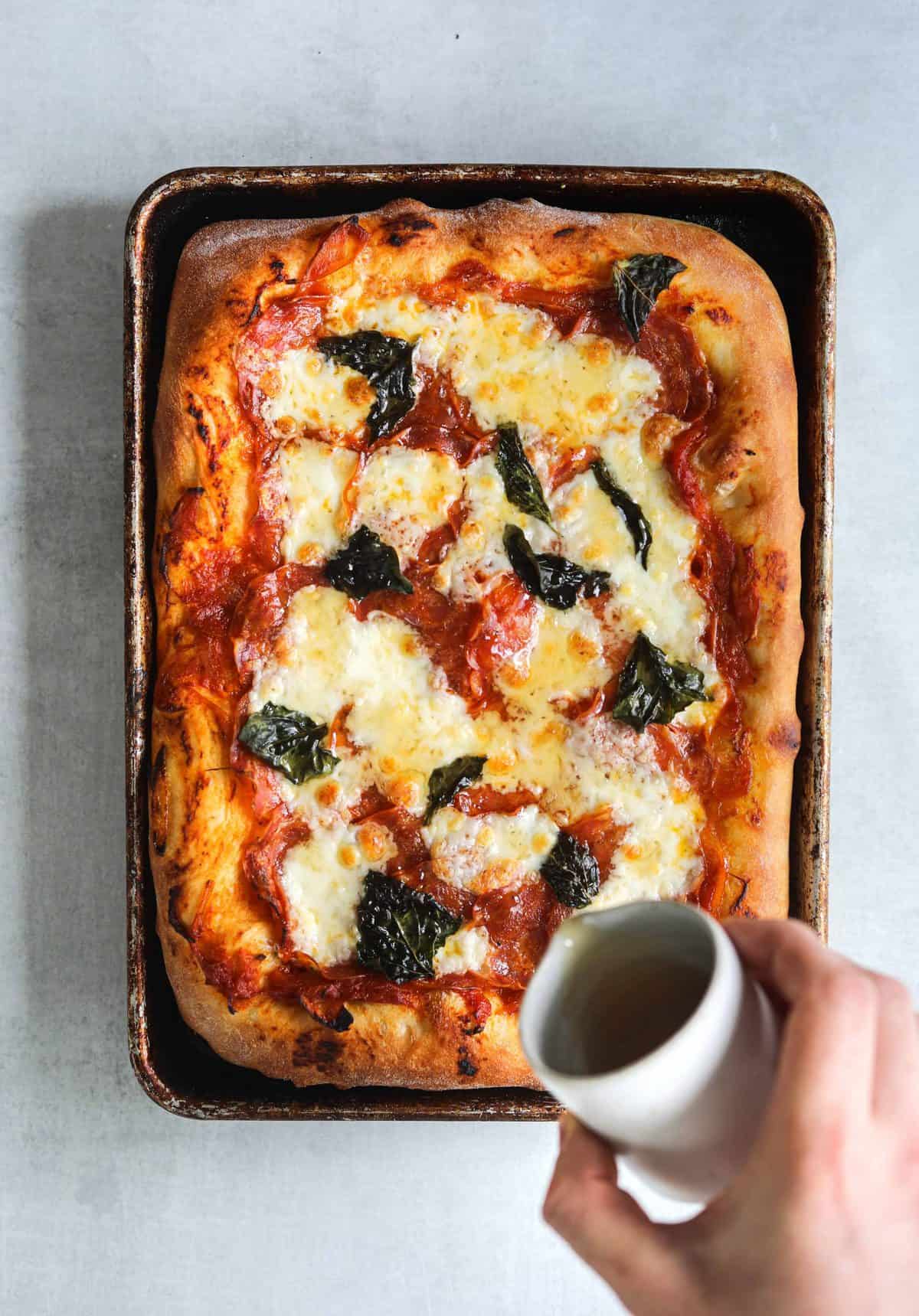 a rectangle pizza on a sheet pan being drizzled with honey