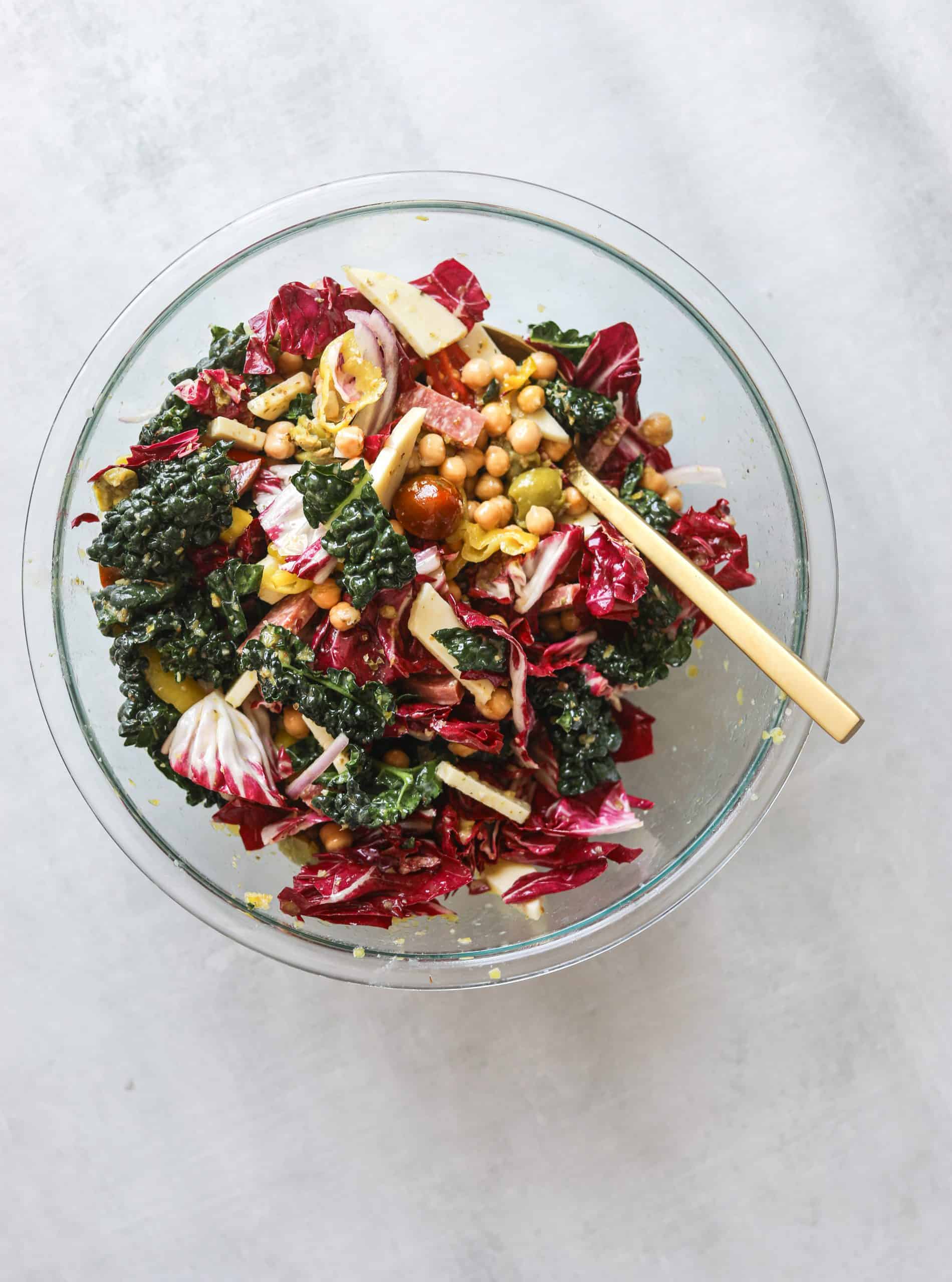 a glass mixing bowl filled with california chopped salad with a gold spoon on a blue background