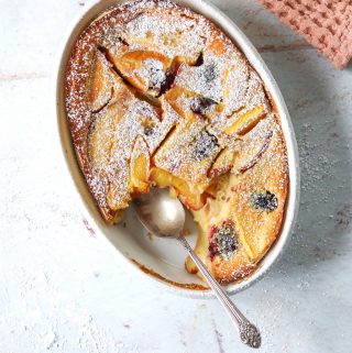 A white oval baking dish filled with Stone Fruit Clafoutis with a silver spoon.