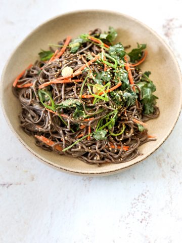 A ceramic bowl filled with Miso-Tahini Soba Noodles topped with sliced scallion and cilantro