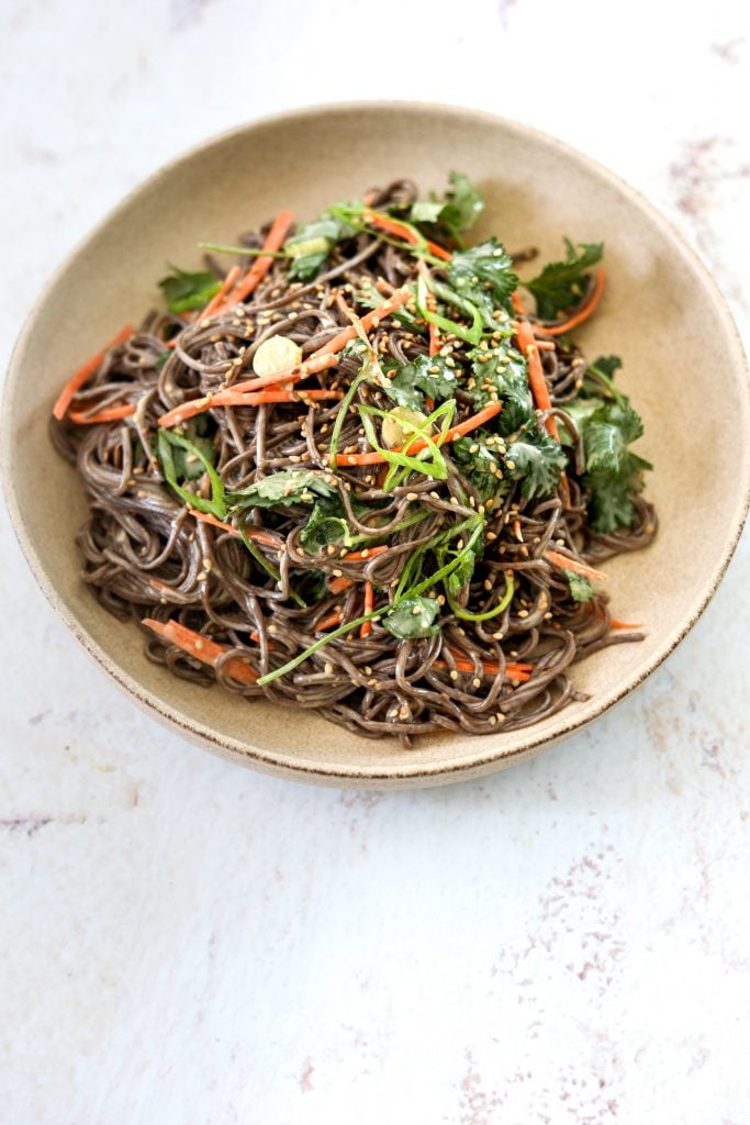 A ceramic bowl filled with Miso-Tahini Soba Noodles topped with sliced scallion and cilantro