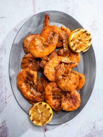 an oval platter filled with grilled shrimp and grilled lemons
