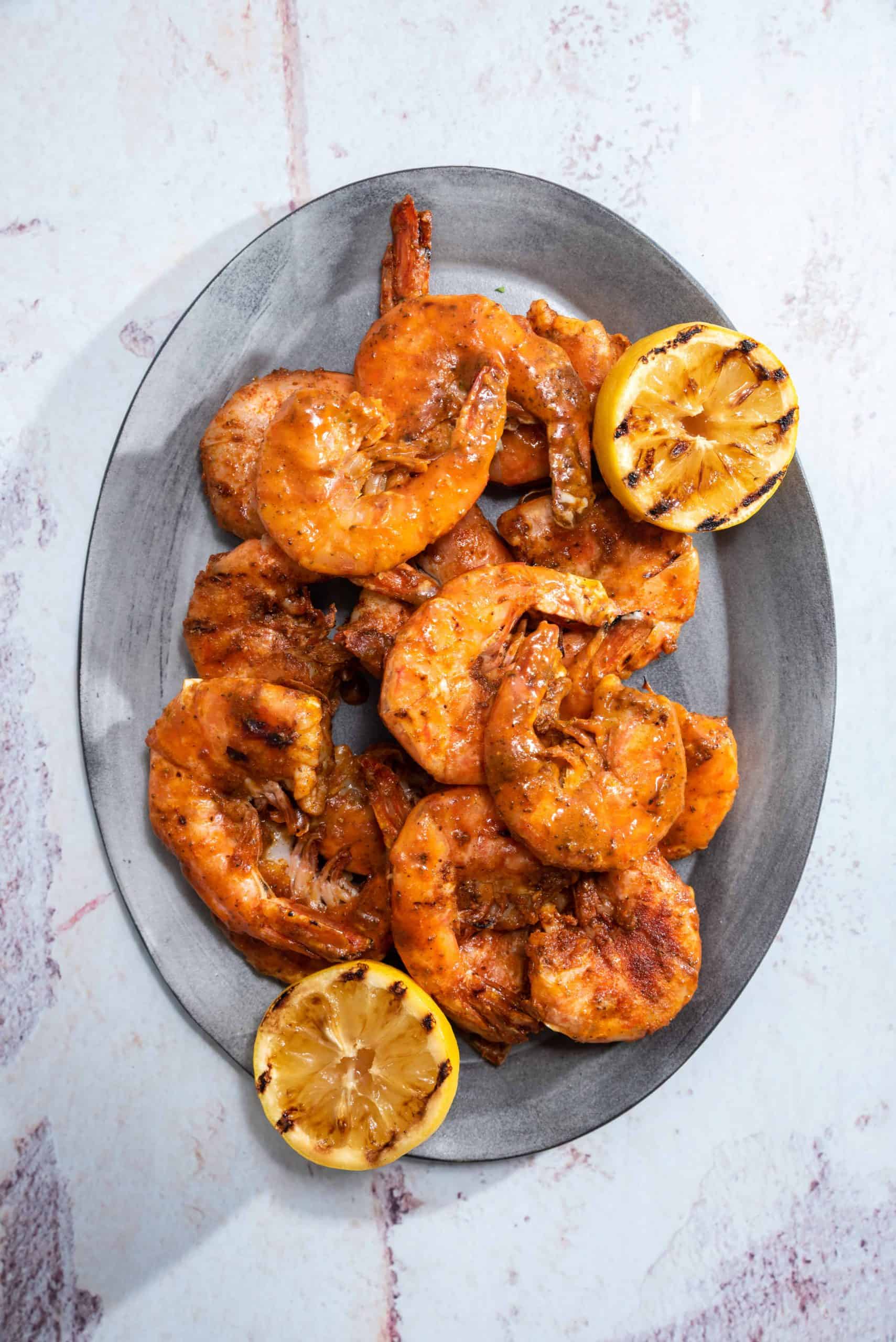 an oval platter filled with grilled shrimp and grilled lemons