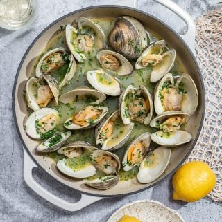 a white pot filled with steamed clams with lemons on the side