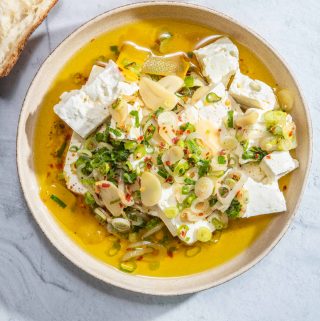 A bowl of marinated feta cheese with olive oil, garlic, shallot and green onion
