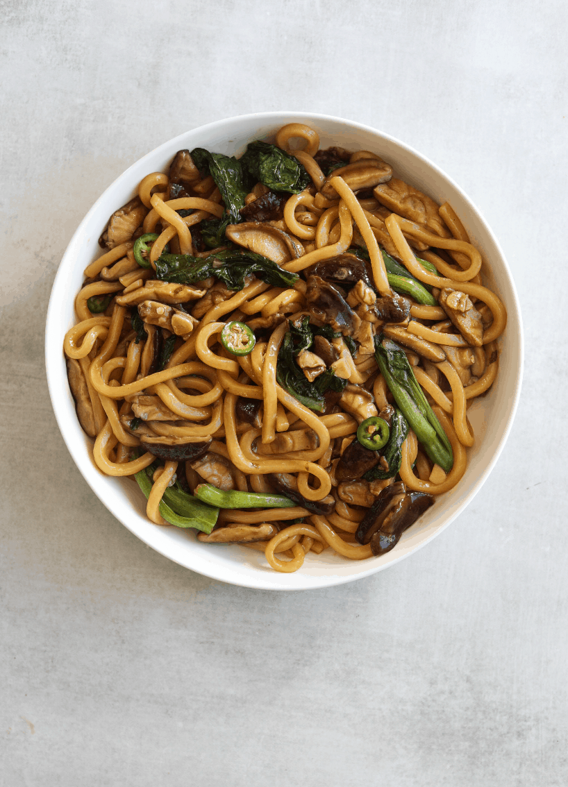 Udon noodle stir fry in a white bowl with mushrooms and broccolini