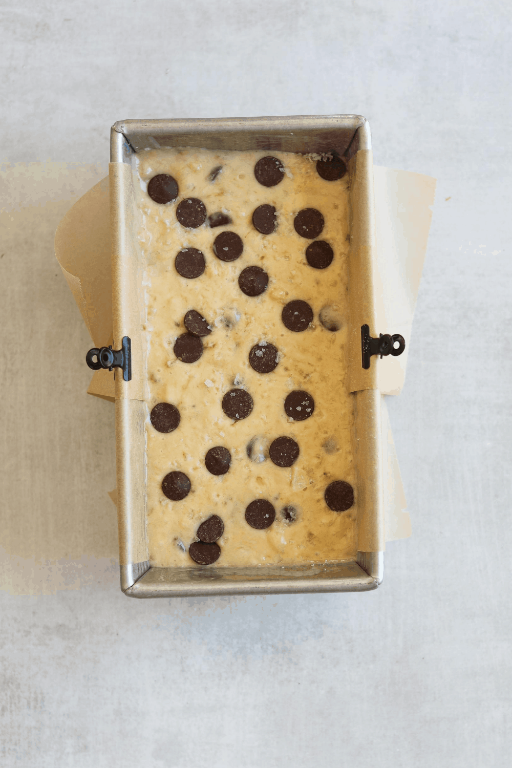 a parchment lined loaf pan filled with banana  bread batter and topped with chocolate chips