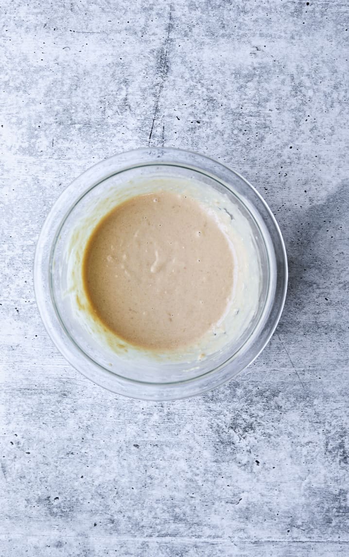 garlic tahini sauce in a glass mixing bowl on a blue background