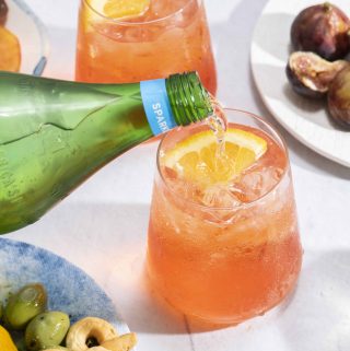 Sparkling water being poured into a bright orange Aperol Spritz cocktail.