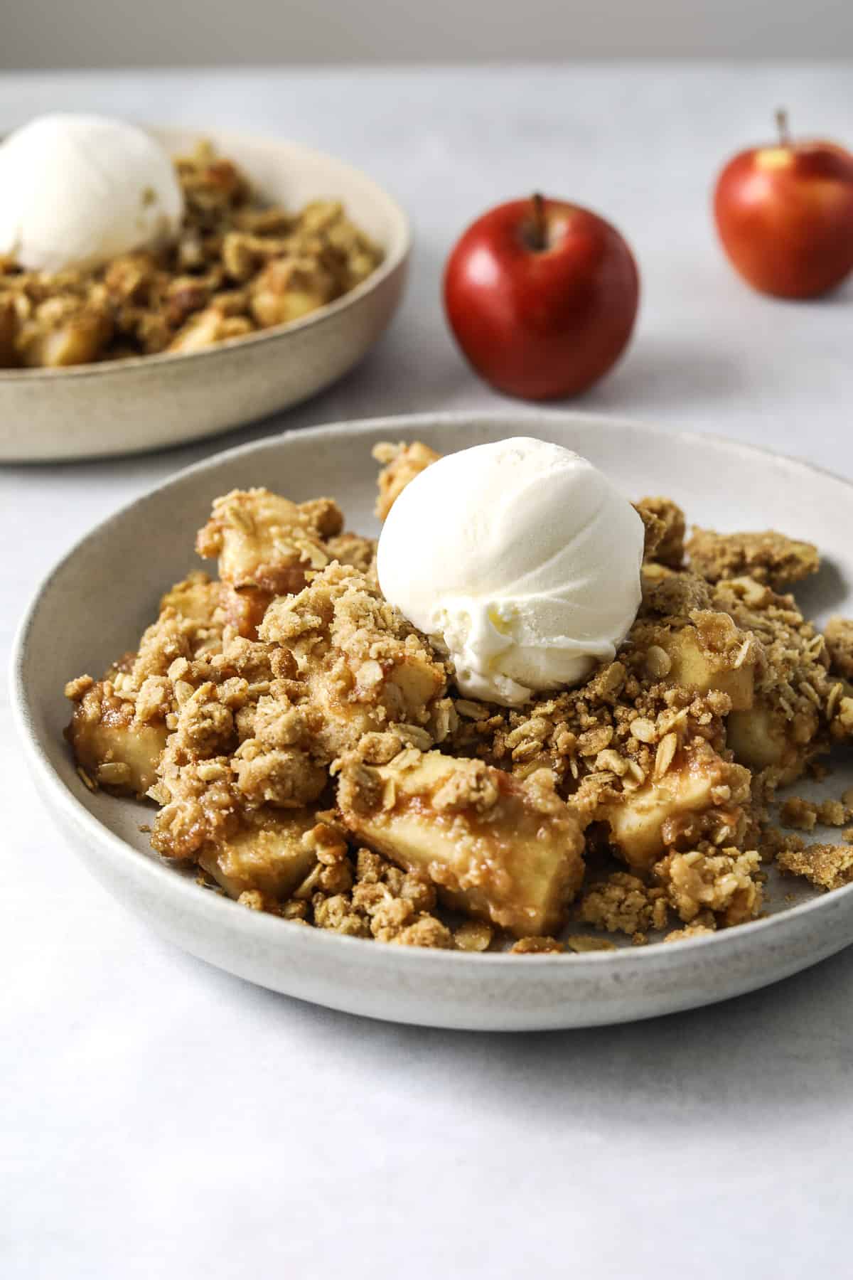 Two bowls of apple crisp topped with a scoop of vanilla ice cream.