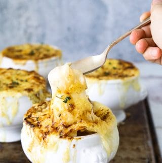 a white crock of vegetarian french onion soup with a spoon dipping into it's melted cheese top