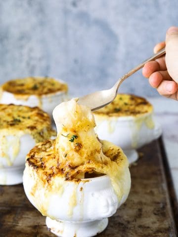 a white crock of vegetarian french onion soup with a spoon dipping into it's melted cheese top