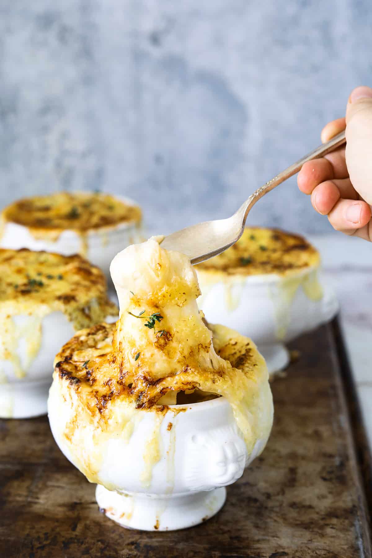 a white crock of vegetarian french onion soup with a spoon dipping into it's melted cheese top 